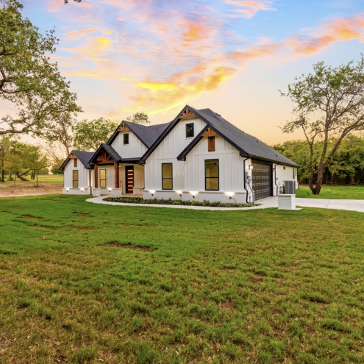 White house twilight photo Modern house with a dark roof and white walls, surrounded by a green lawn and sunset sky.