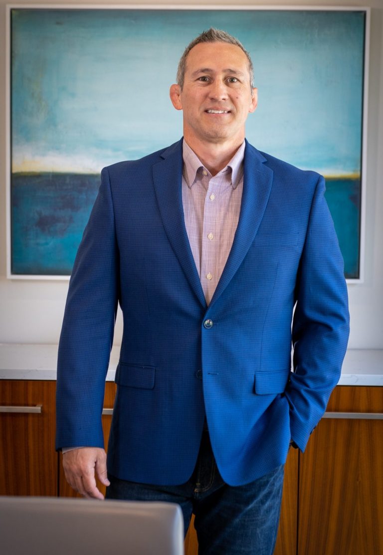 Capture & Close Real Estate Imagery Owner Man in a blue suit standing in front of a large abstract painting. Chad McPhatter